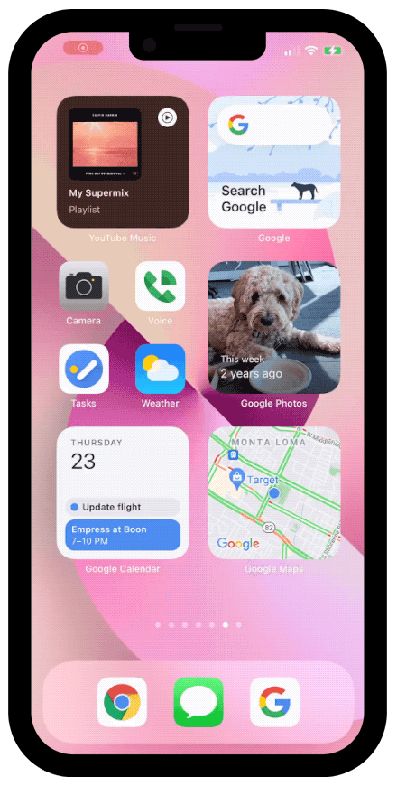 An iPhone 13 screen with a pink background showing a user dragging different Google widgets over one another to build a new Smart Stack.