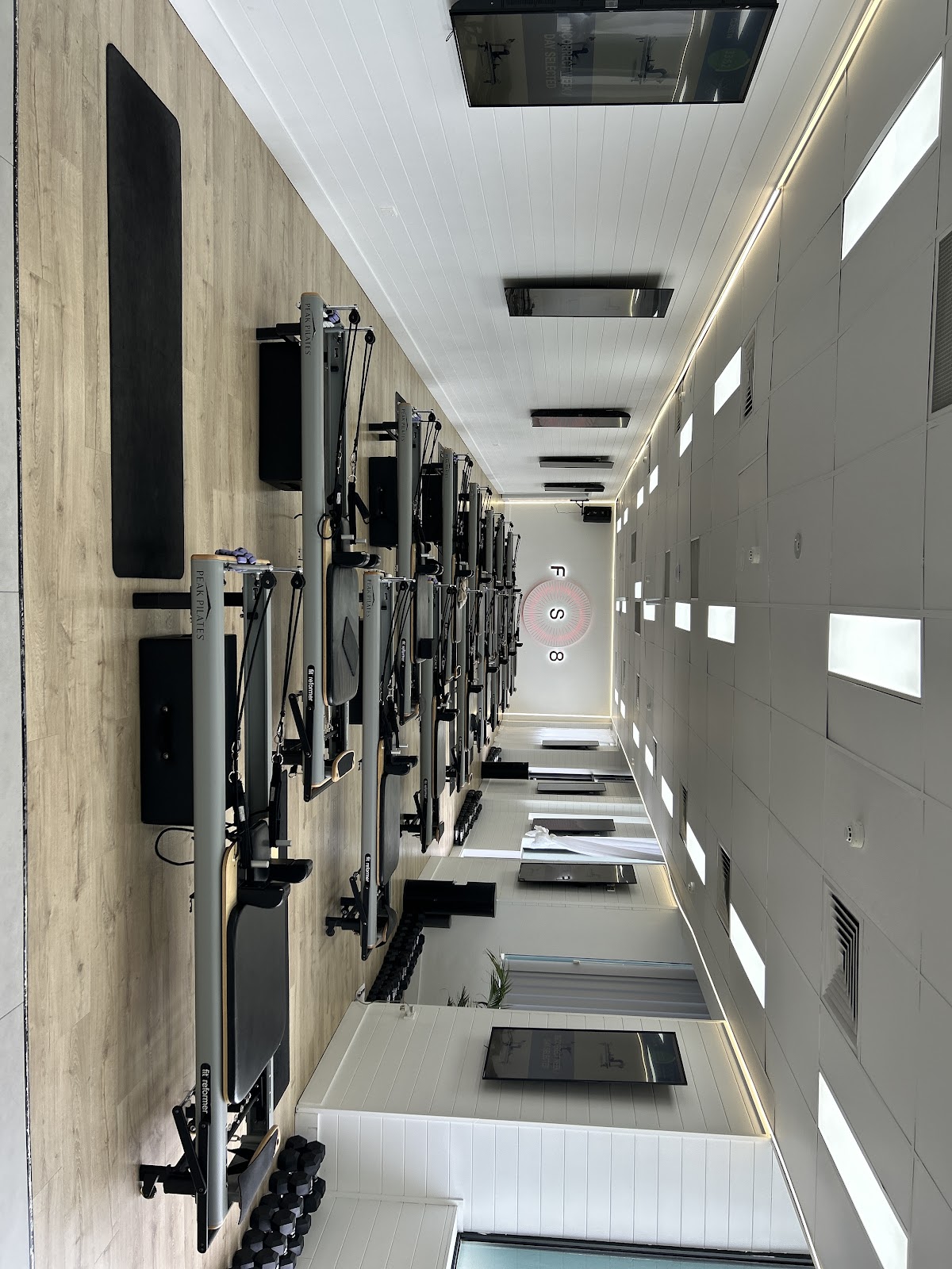 This photo shows a clean, minimalist studio with multiple reformer pilates machines lined up along a hallway.