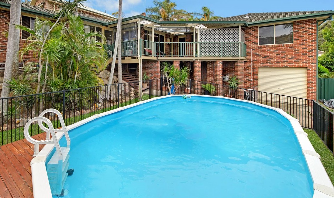 This photo showcases a swimming pool as an amenity of a brick house with lush greenery surrounding it.