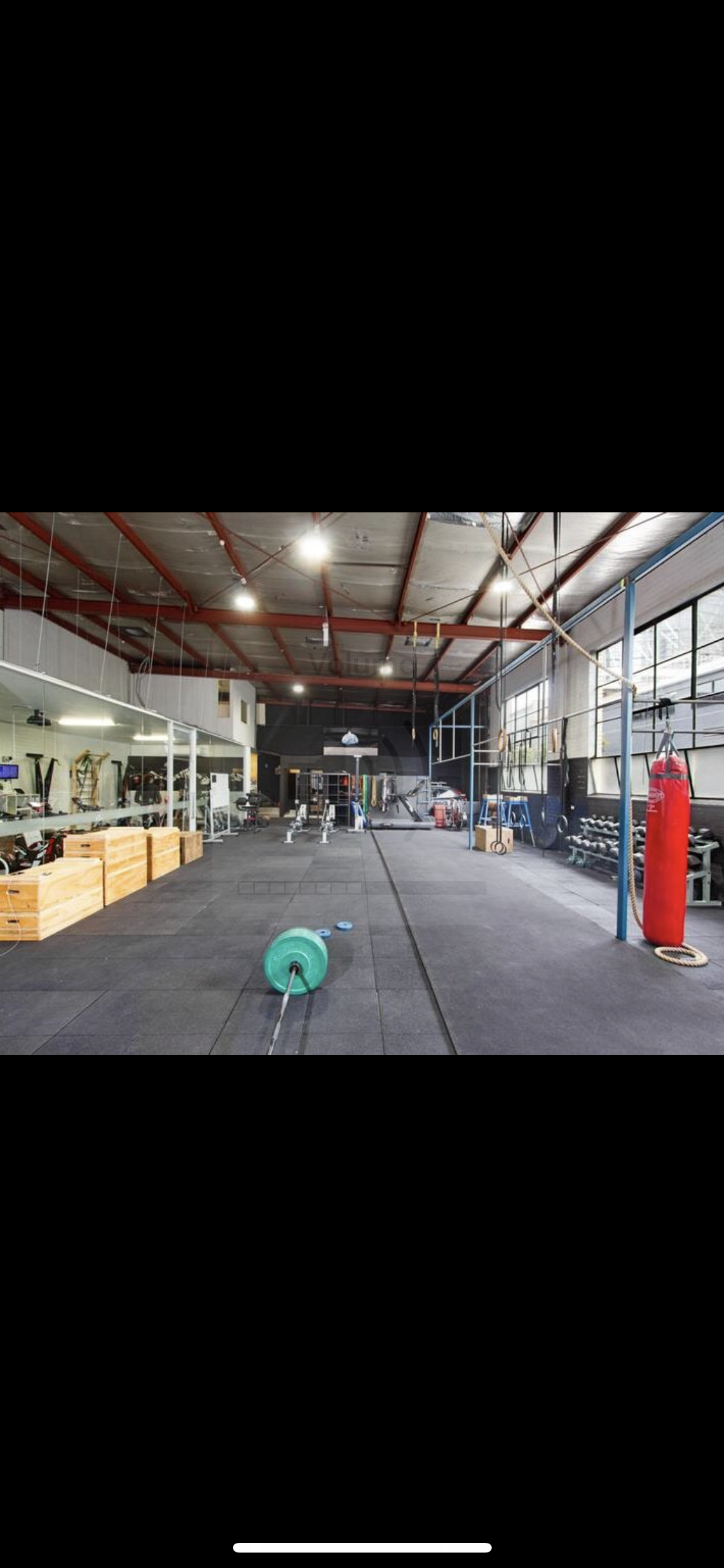 The photo shows a large, industrial-style gym floor with free weights, squat racks, and boxing bags.