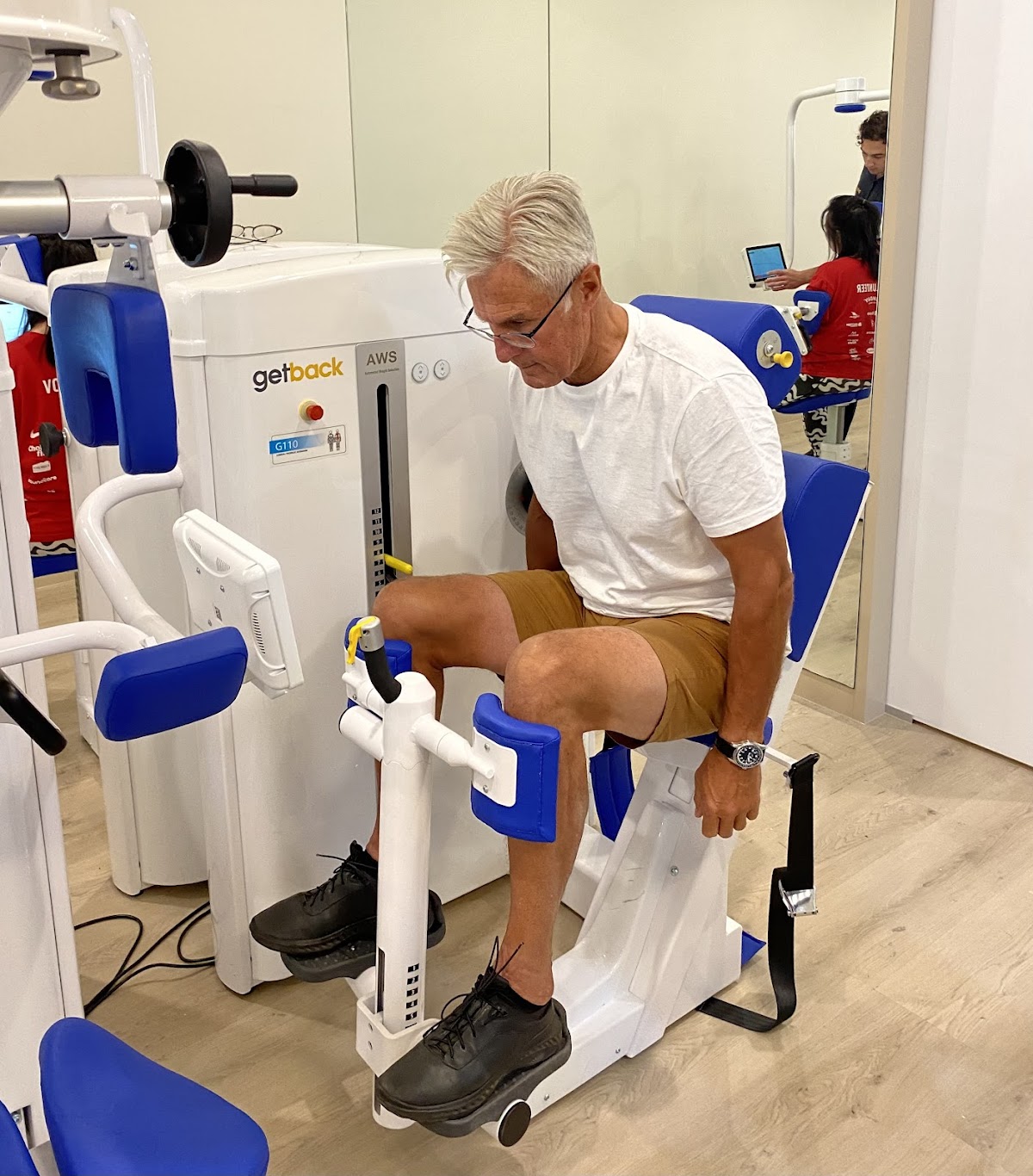 An older man is using a specialized rehabilitation machine in what appears to be a clinical fitness setting.