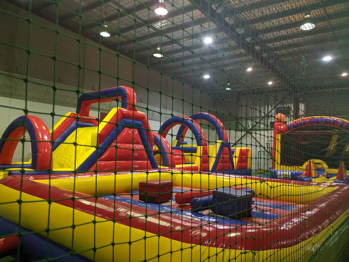 The photo shows a large indoor play area with a climbing wall and inflatable obstacles, likely for children.