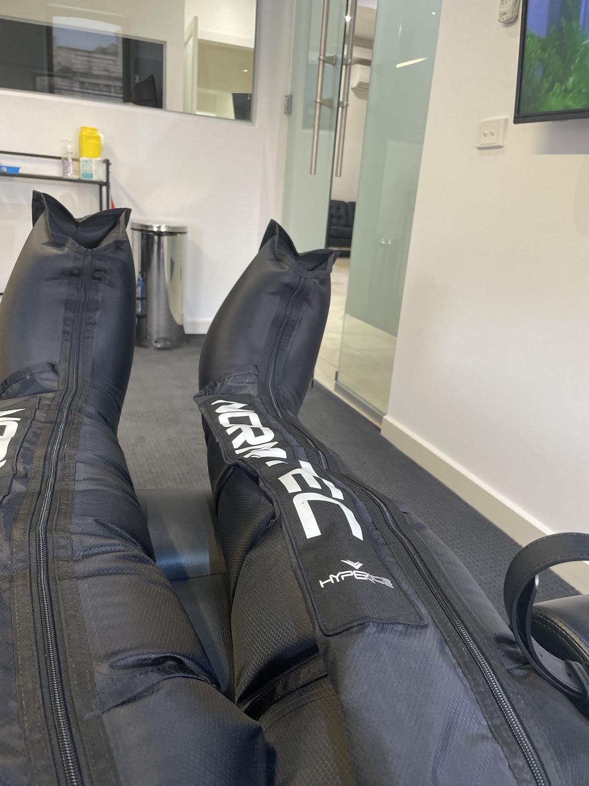 The photo showcases a close-up of NormaTec recovery boots in a modern fitness facility setting.