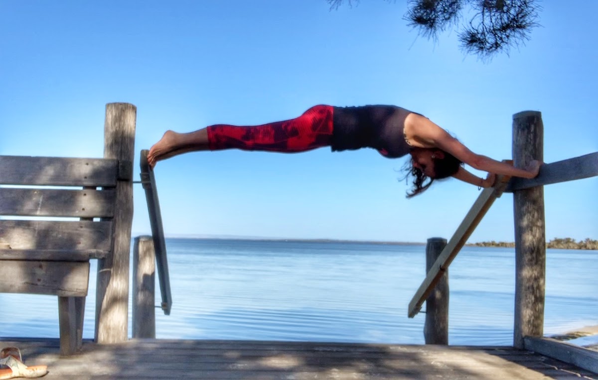 A woman performs a yoga pose on a wooden structure overlooking a body of water.