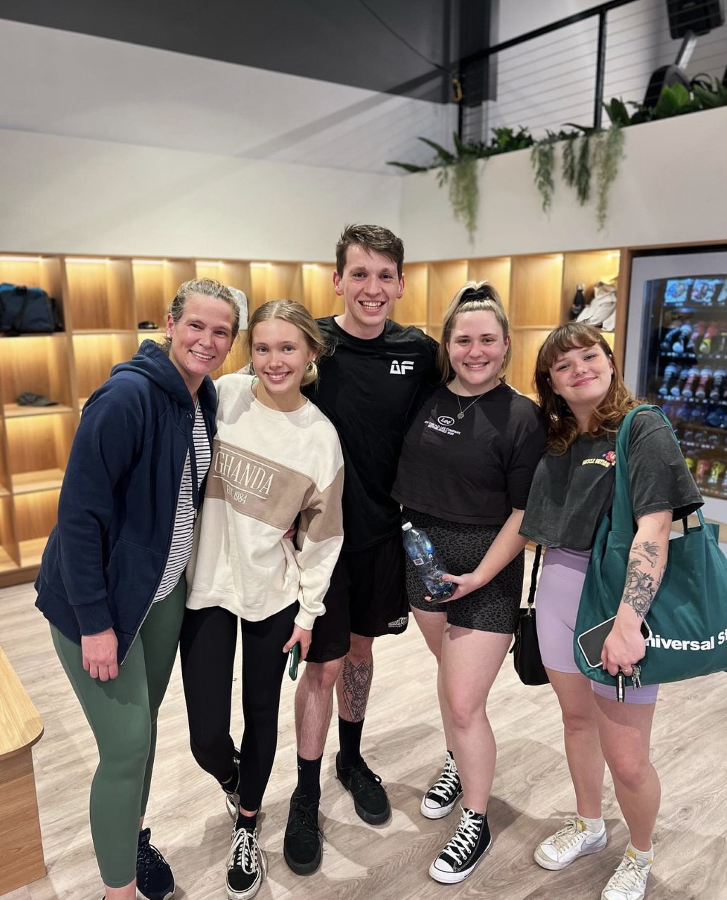 A group of five people, including a trainer, are posing for a photo in a brightly lit fitness studio.