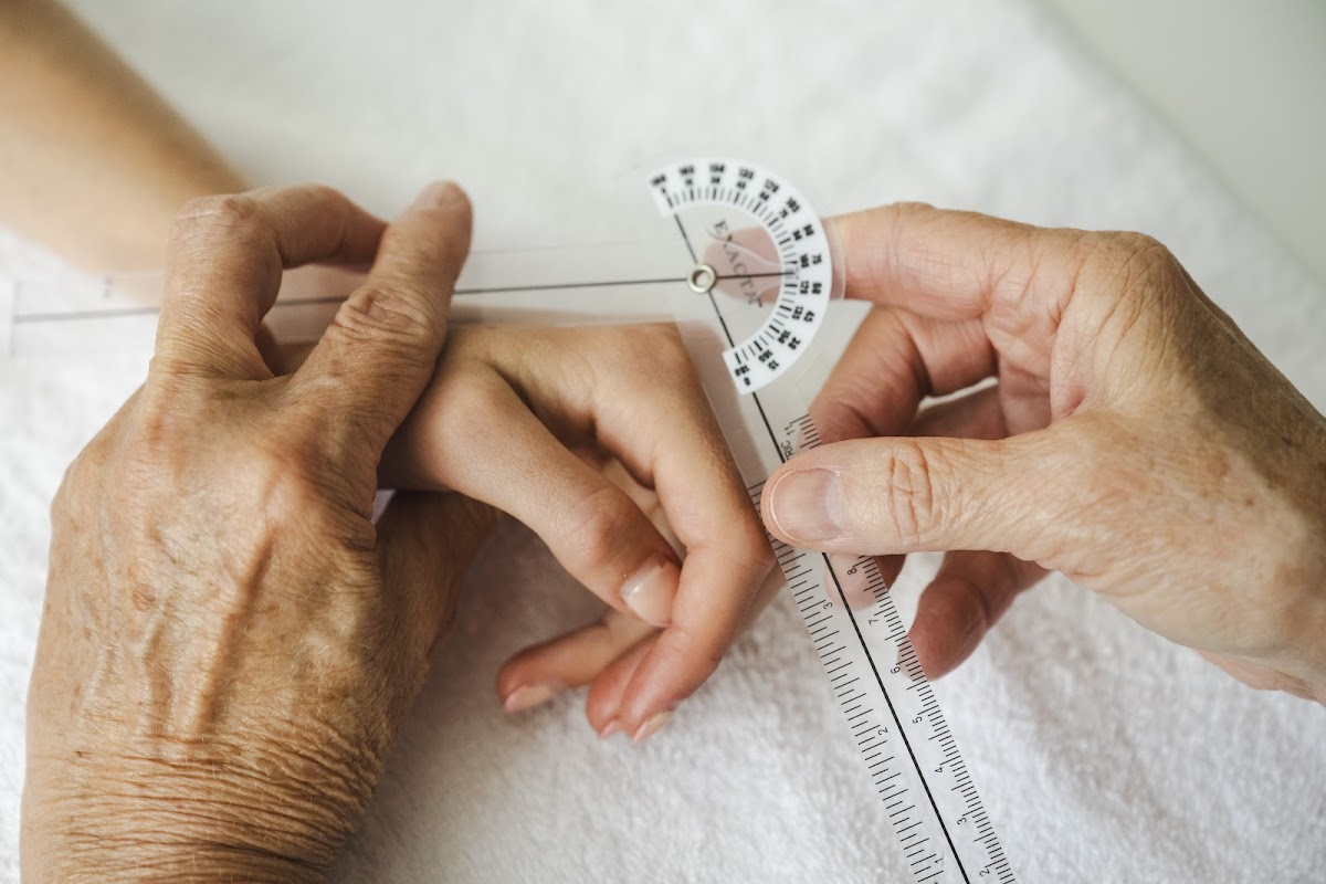 An older person's hands are being assessed with a goniometer on a yoga mat.