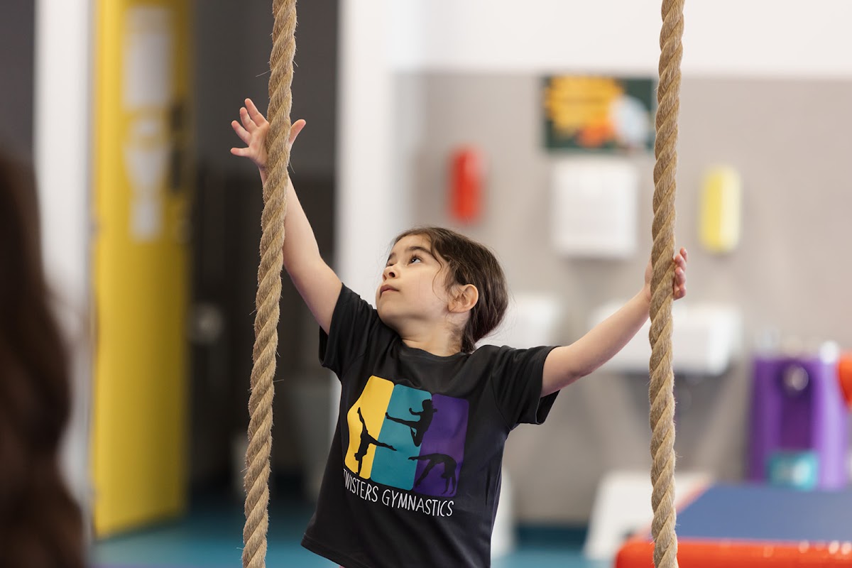 A young girl is hanging from ropes in a gymnastics gym, showcasing a children's training program.