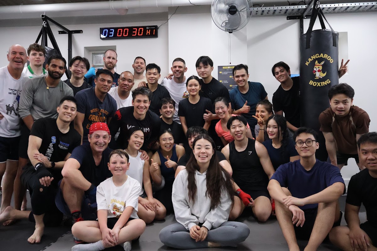 A large group of people, including children, are posing for a photo in a boxing gym setting.