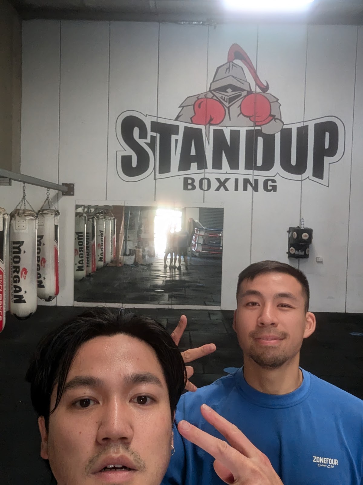 A man poses in front of a boxing gym with punching bags and the 'Standup Boxing' logo.