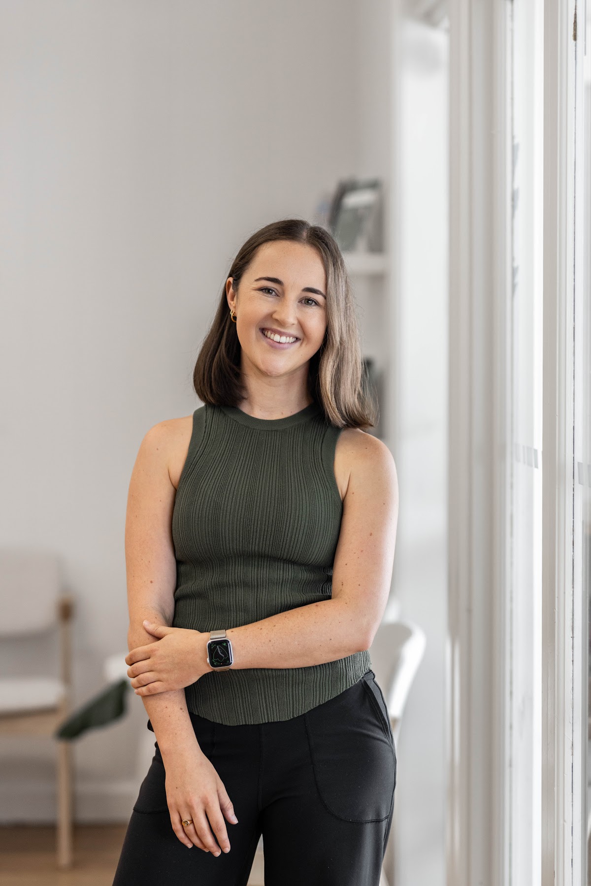 A smiling female trainer stands confidently in a minimalist studio setting.