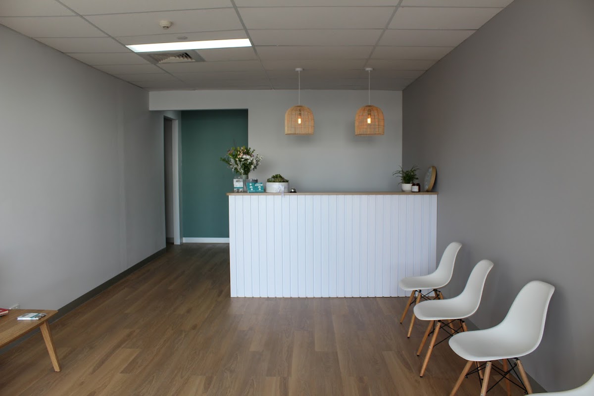 This photo shows a clean and minimalist reception area of a fitness business with a white reception desk and chairs.