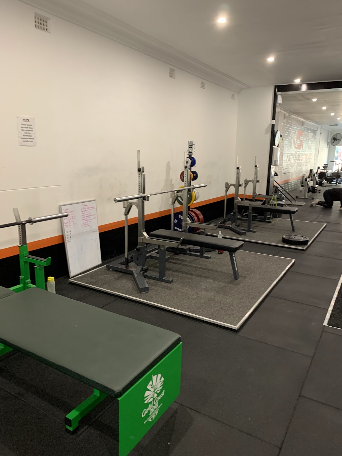 The photo shows a gym floor with several squat racks and benches set up for powerlifting or strength training.