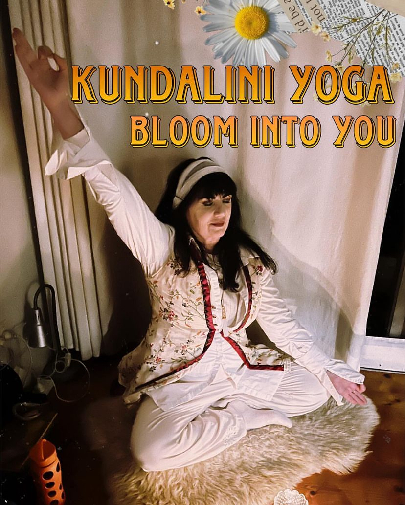 A woman in yoga attire is demonstrating a pose on a yoga mat in a dimly lit studio with a floral-themed sign.