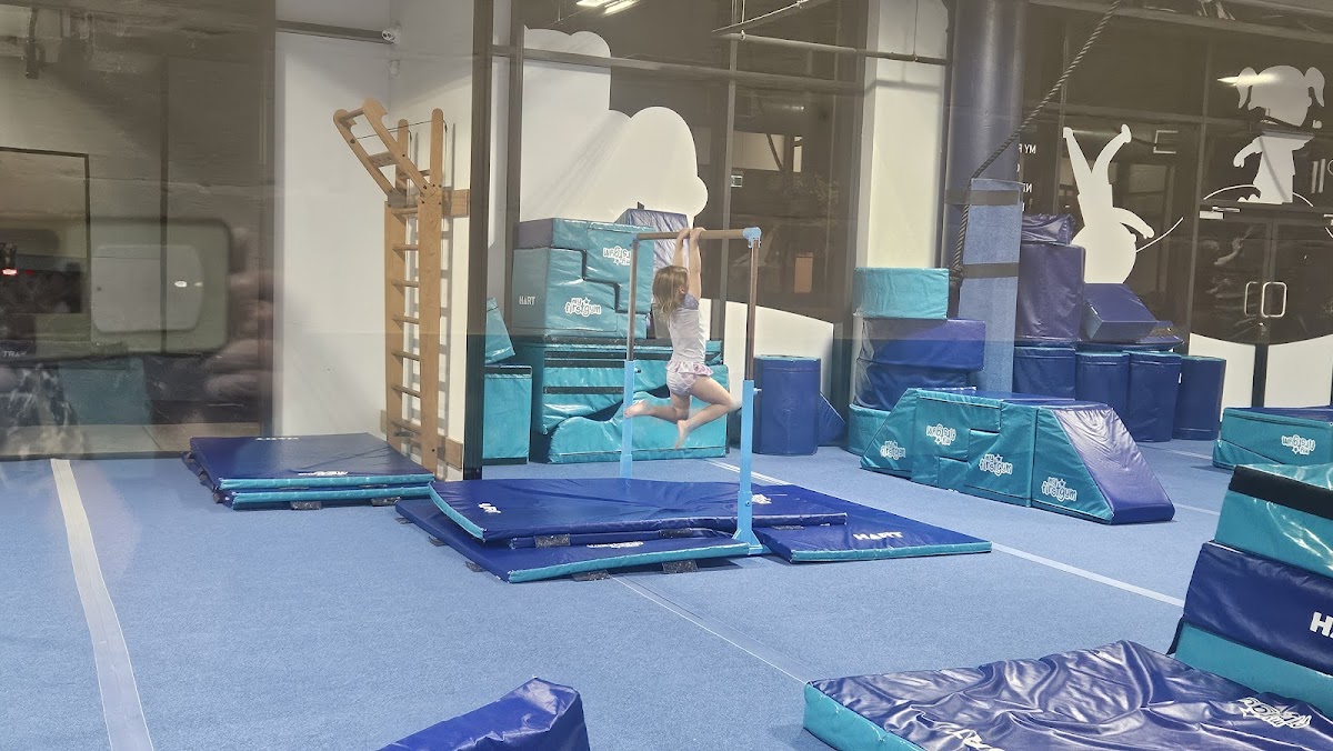 A young person is performing a gymnastic move on a climbing wall and mats in a dimly lit gym.
