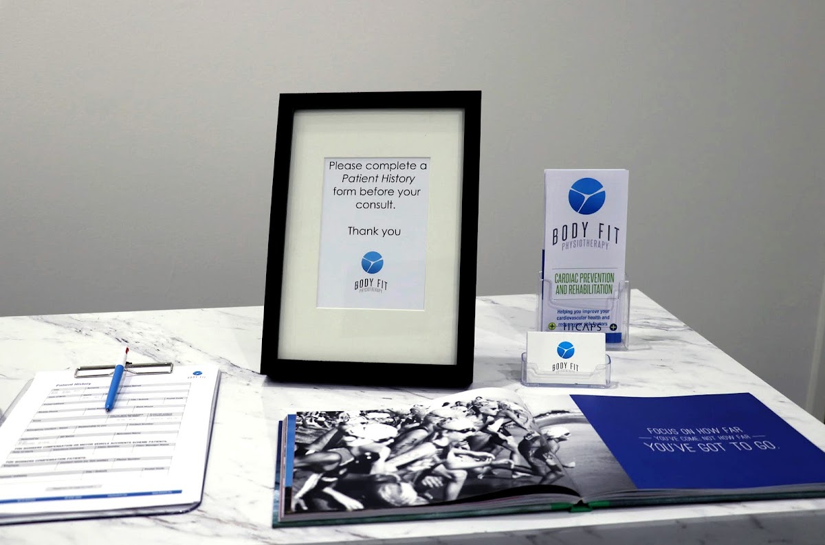 The photo shows a physiotherapy clinic reception area with paperwork and weights on a table.
