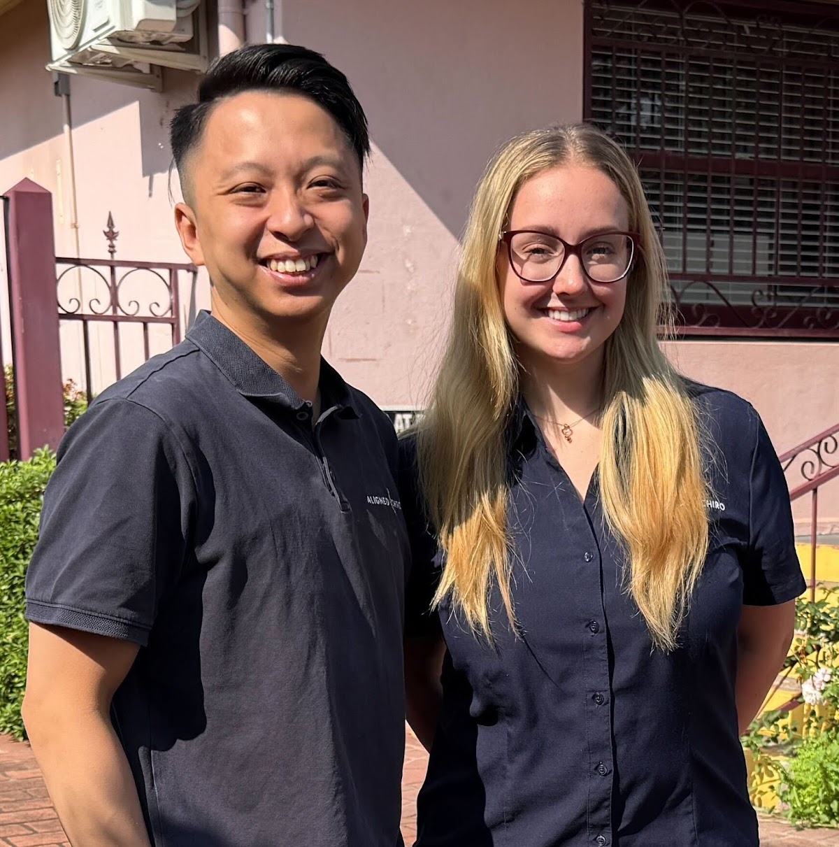 Two smiling trainers, a man and a woman, pose for a portrait in front of a building.
