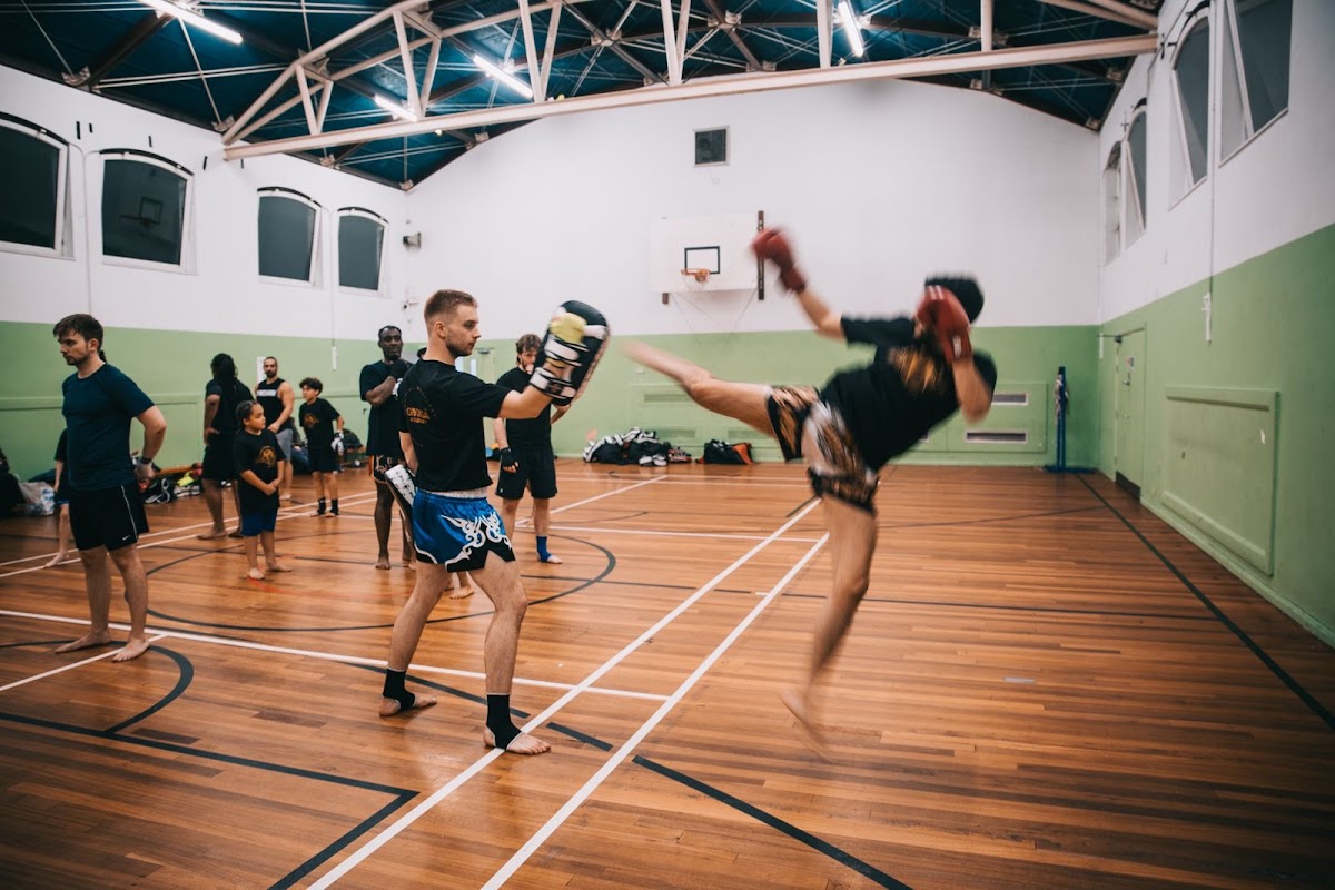 A mixed group of men are participating in a boxing training session with a male trainer in an indoor gym setting.