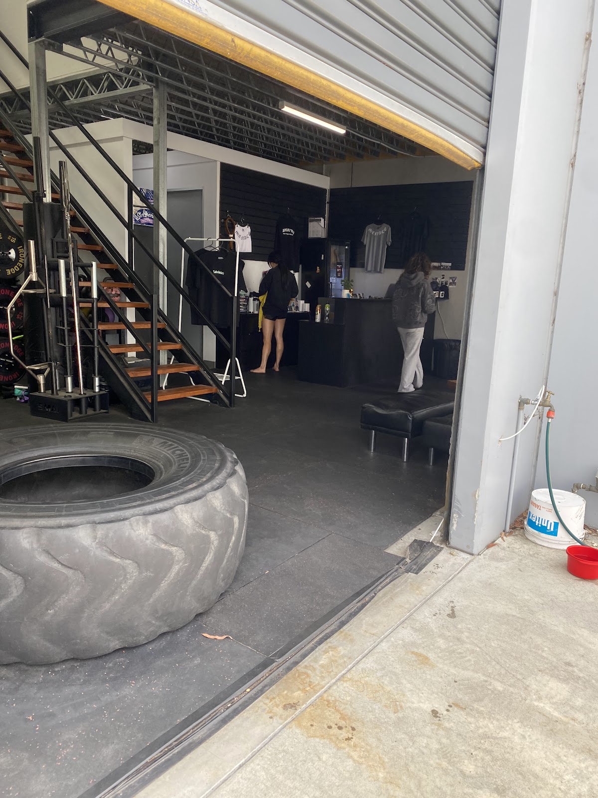 The photo shows a dimly lit interior gym floor with powerlifting equipment and free weights visible, suggesting a focus on strength training.