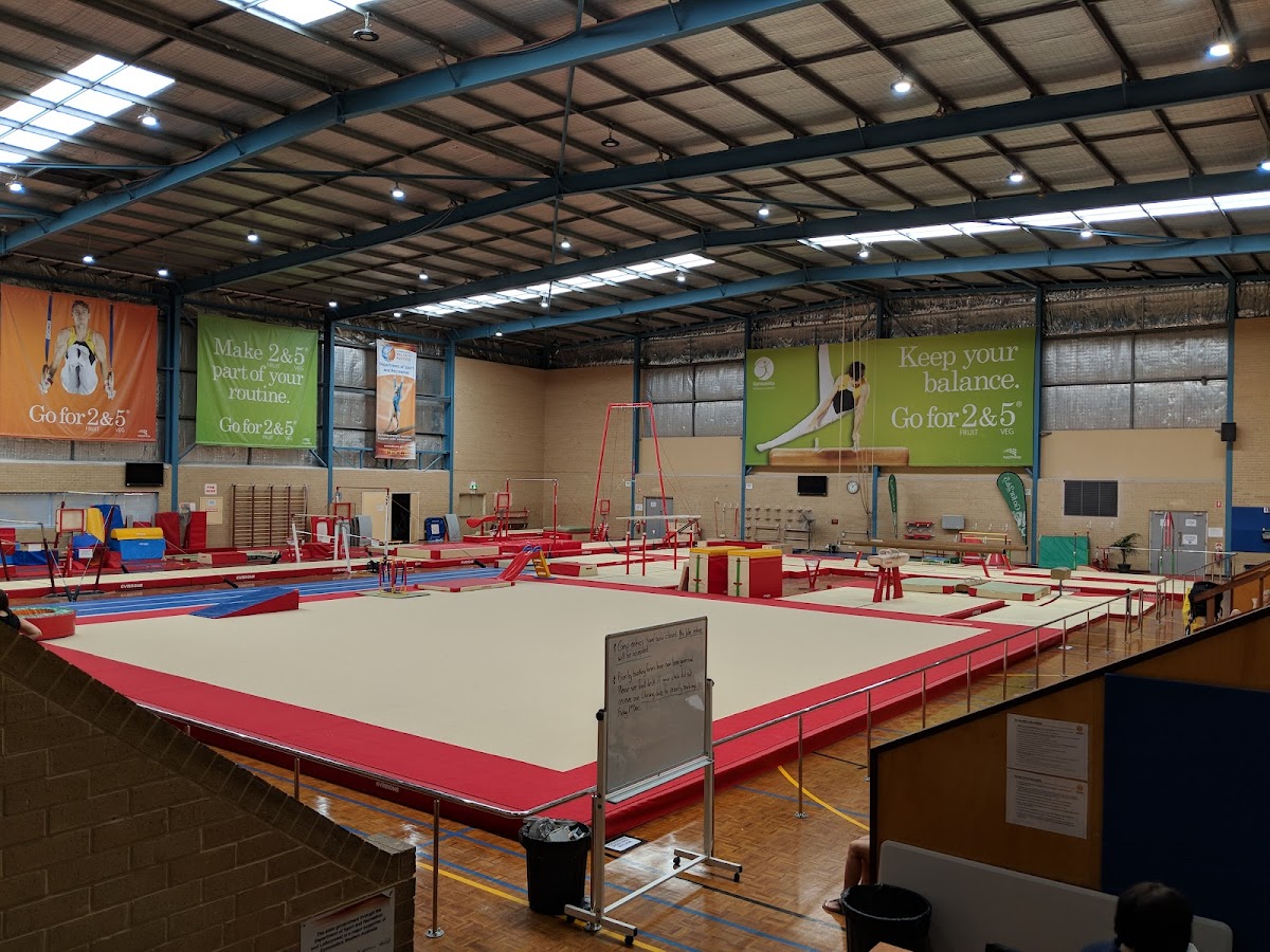 This photo shows a large, industrial-style gym floor with gymnastic equipment and free weights, likely used for strength training and gymnastics.