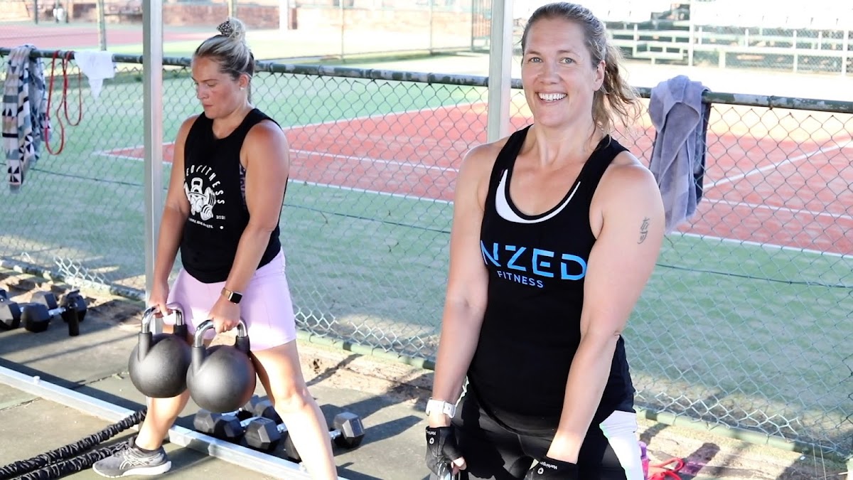 Two women are performing kettlebell squats during an outdoor fitness class.