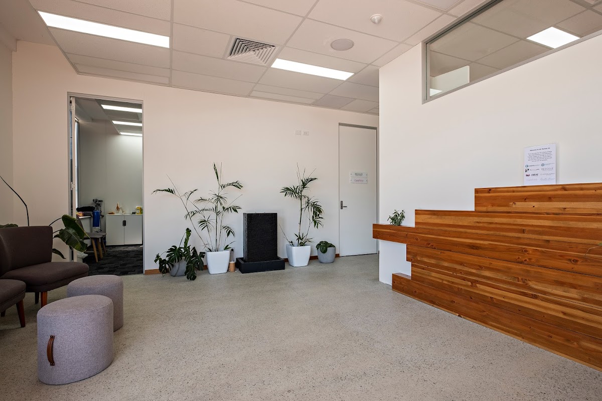 This photo shows a clean and minimalist reception area of a fitness business with seating and a wooden desk.