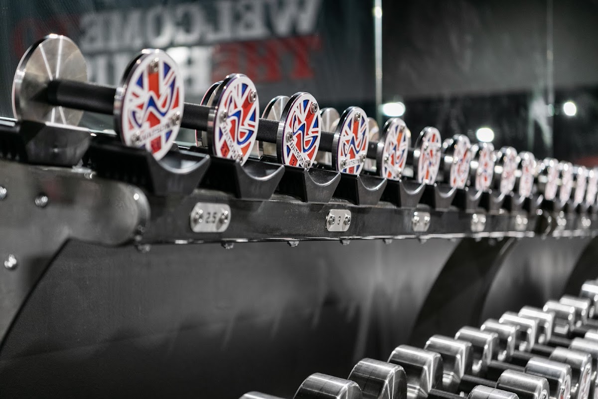 A close-up shot showcases a row of squat racks with free weights and the 'Metcon' logo visible in the background.