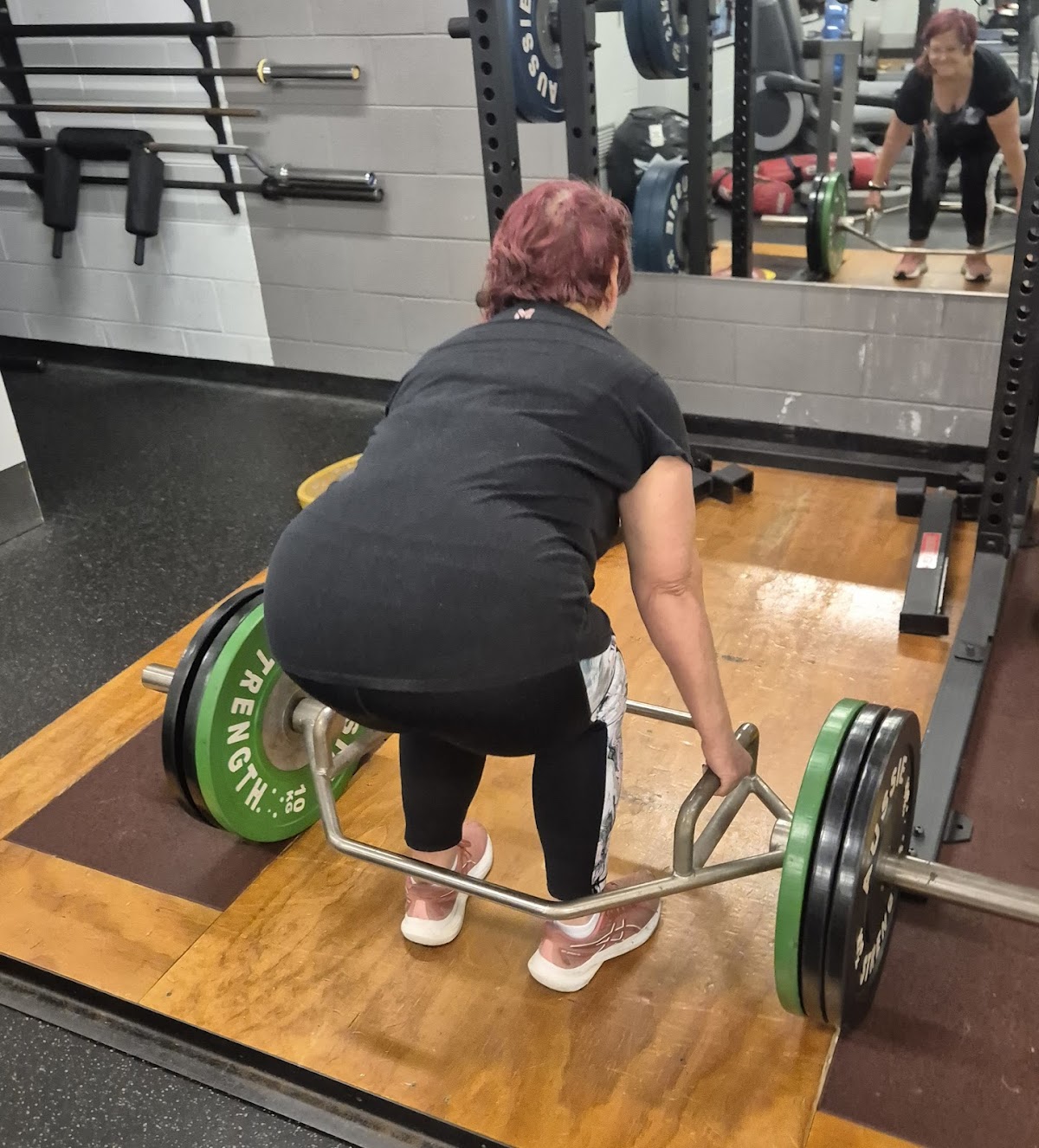 A woman is performing a deadlift with a barbell in a gym setting.