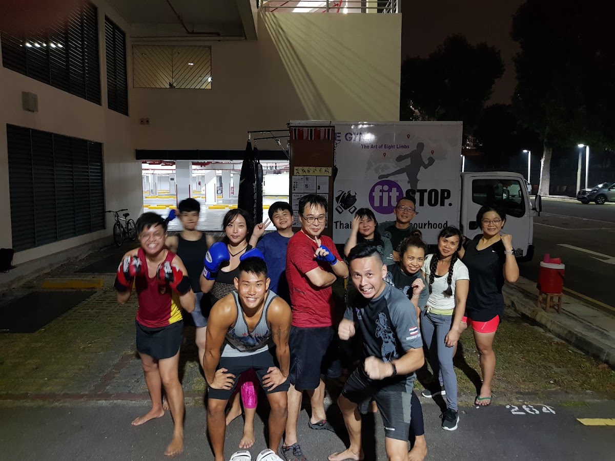 A group of people, including trainers, are posing for a photo outside a gym, likely after a workout session.