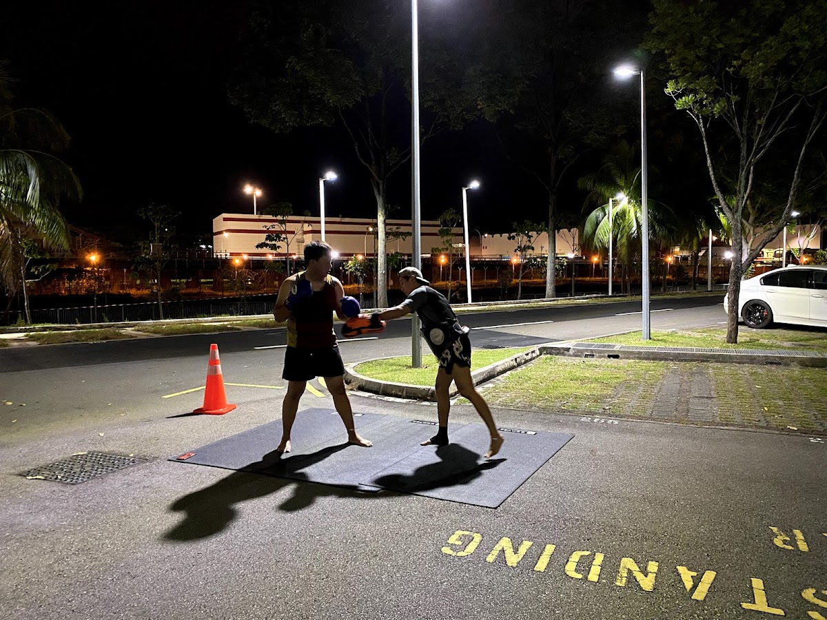 Two individuals are engaged in a boxing training session outdoors at night under streetlights.