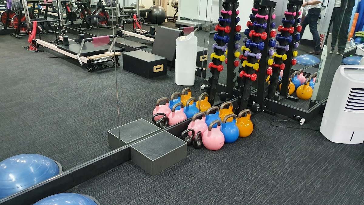 The photo shows a gym floor with free weights, kettlebells, squat racks and TRX suspension trainers.