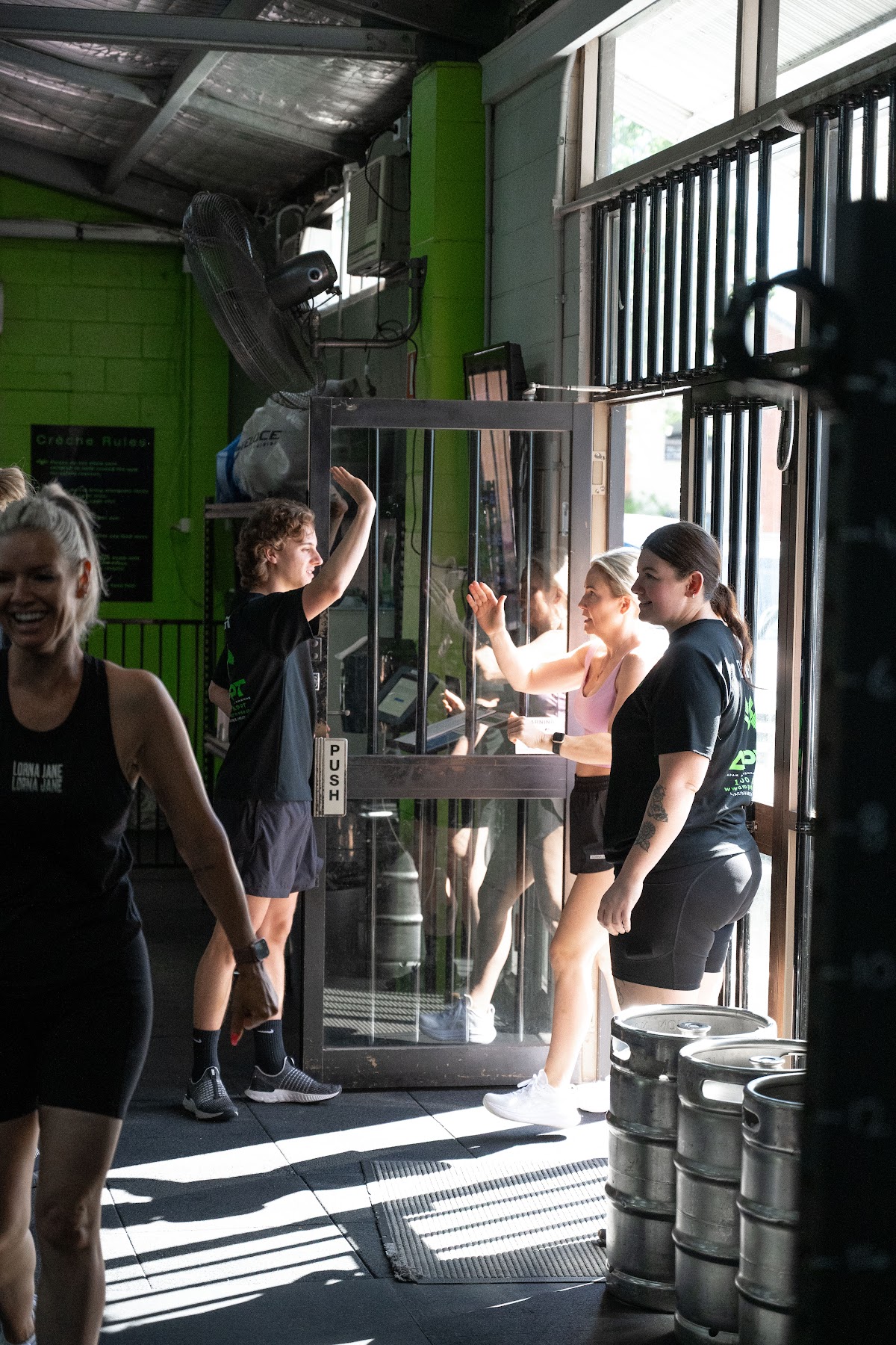 A group fitness class is taking place in a gritty gym setting with visible climbing wall and free weights.