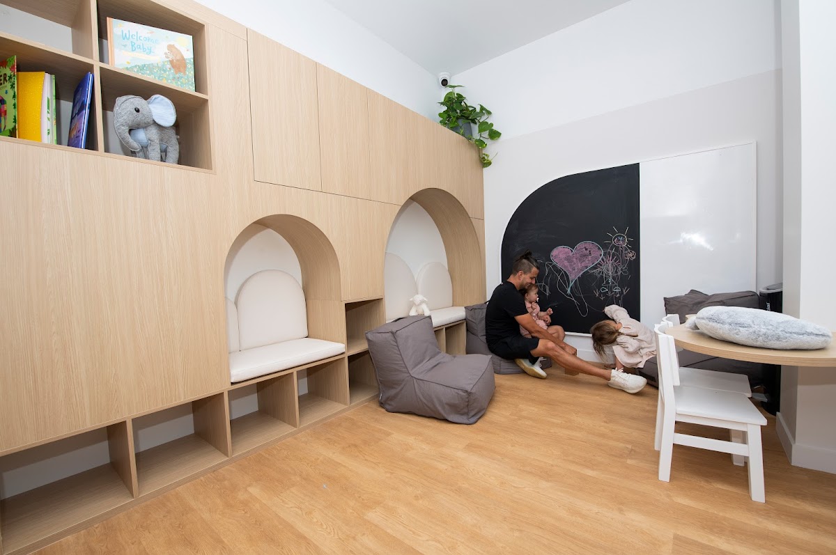 The photo shows a light-filled studio space with wooden shelving, a chalkboard wall with drawings, and a comfortable seating area with a beanbag chair