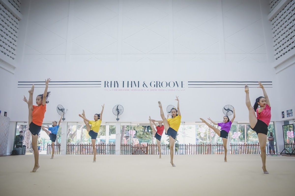 A group of dancers in colorful outfits perform a synchronized routine in a spacious, brightly lit studio.