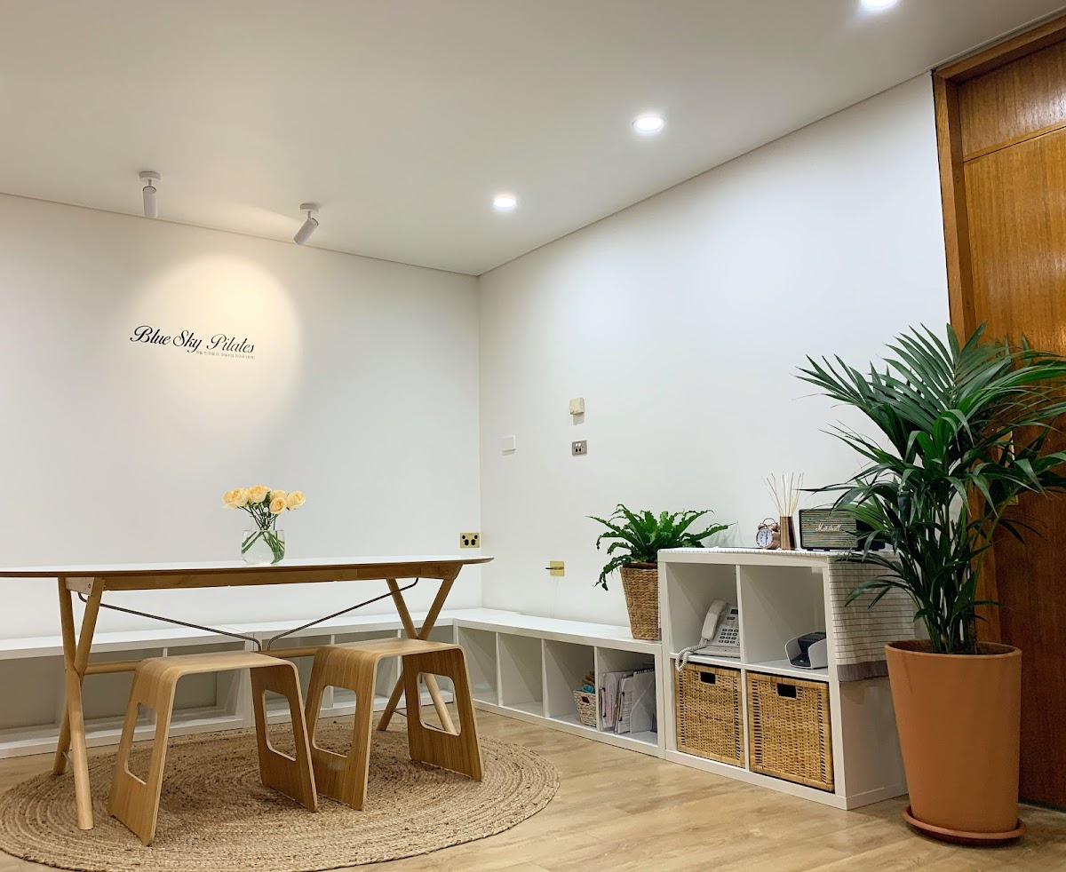 This photo shows a clean and minimalist studio space with wooden furniture, plants, and a sign indicating it is a Pilates studio.