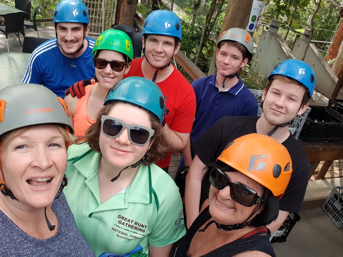 A group of people wearing safety helmets and gear are posing for a photo in an outdoor adventure park setting.