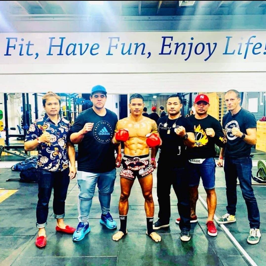 A group of individuals including trainers pose with a fighter in boxing gear within a gym setting.