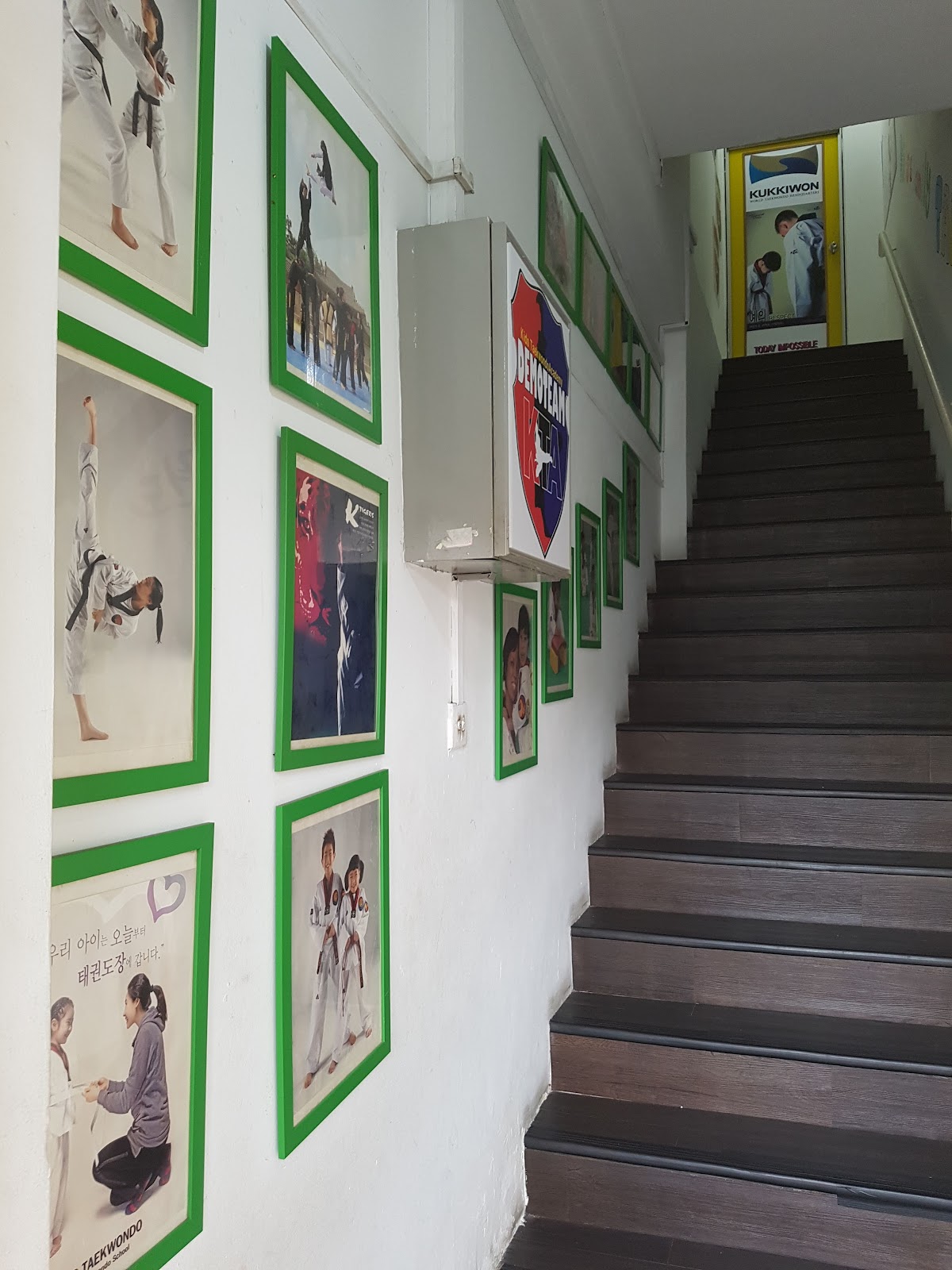 A hallway with stairs leads up, decorated with framed Taekwondo posters and artwork.
