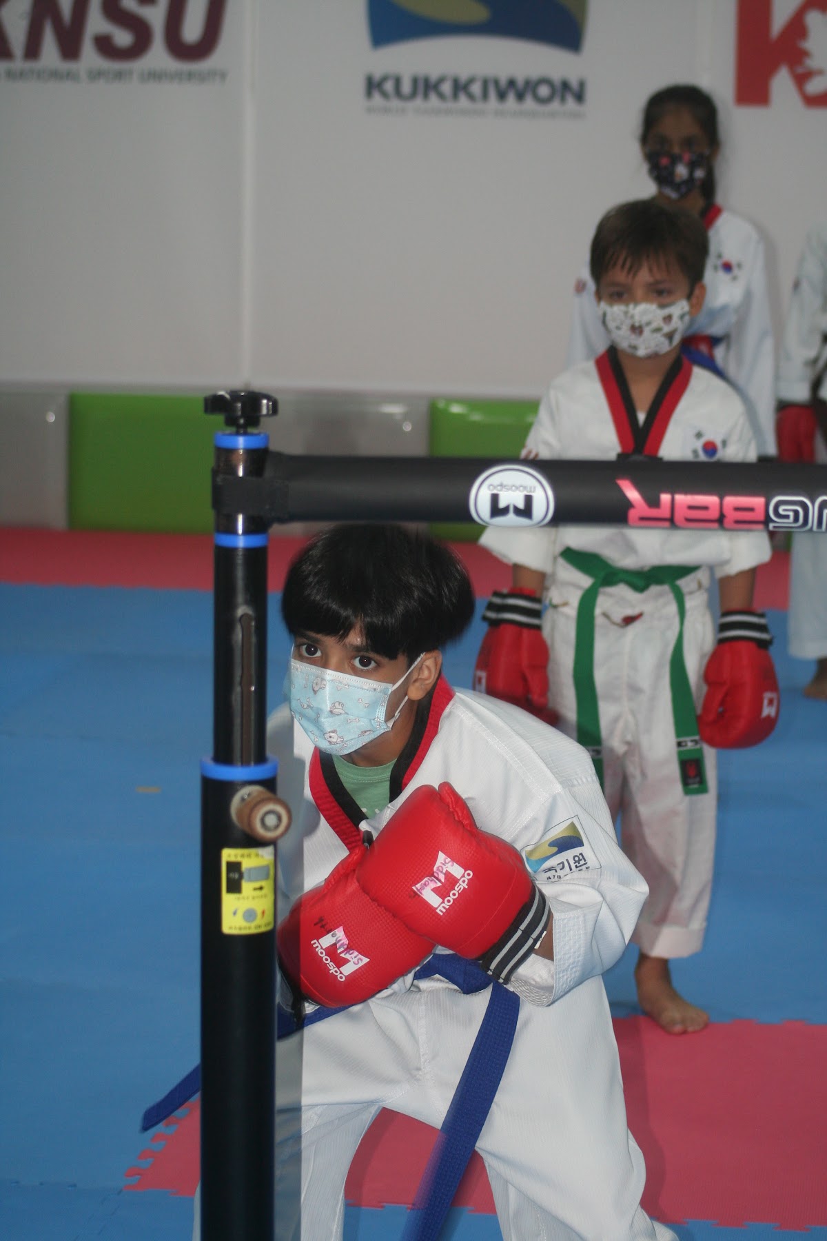 A group of young children are practicing martial arts techniques with a punching bag in what appears to be a training facility.