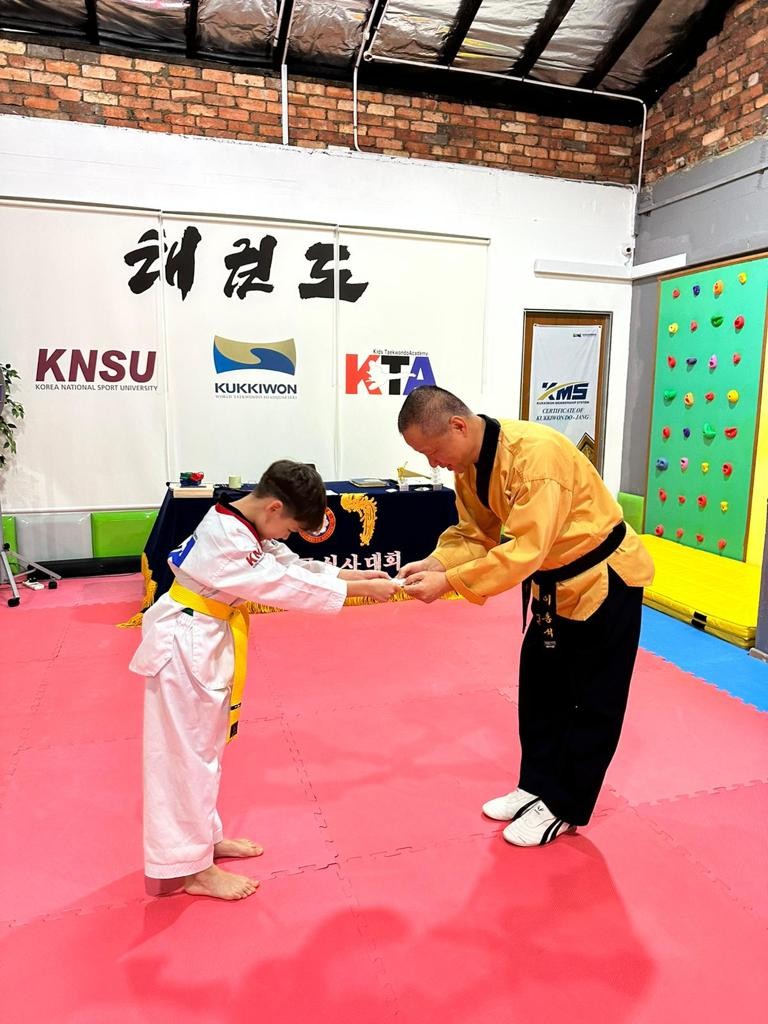 A male trainer is instructing a young student in martial arts on mats within an industrial-style gym.