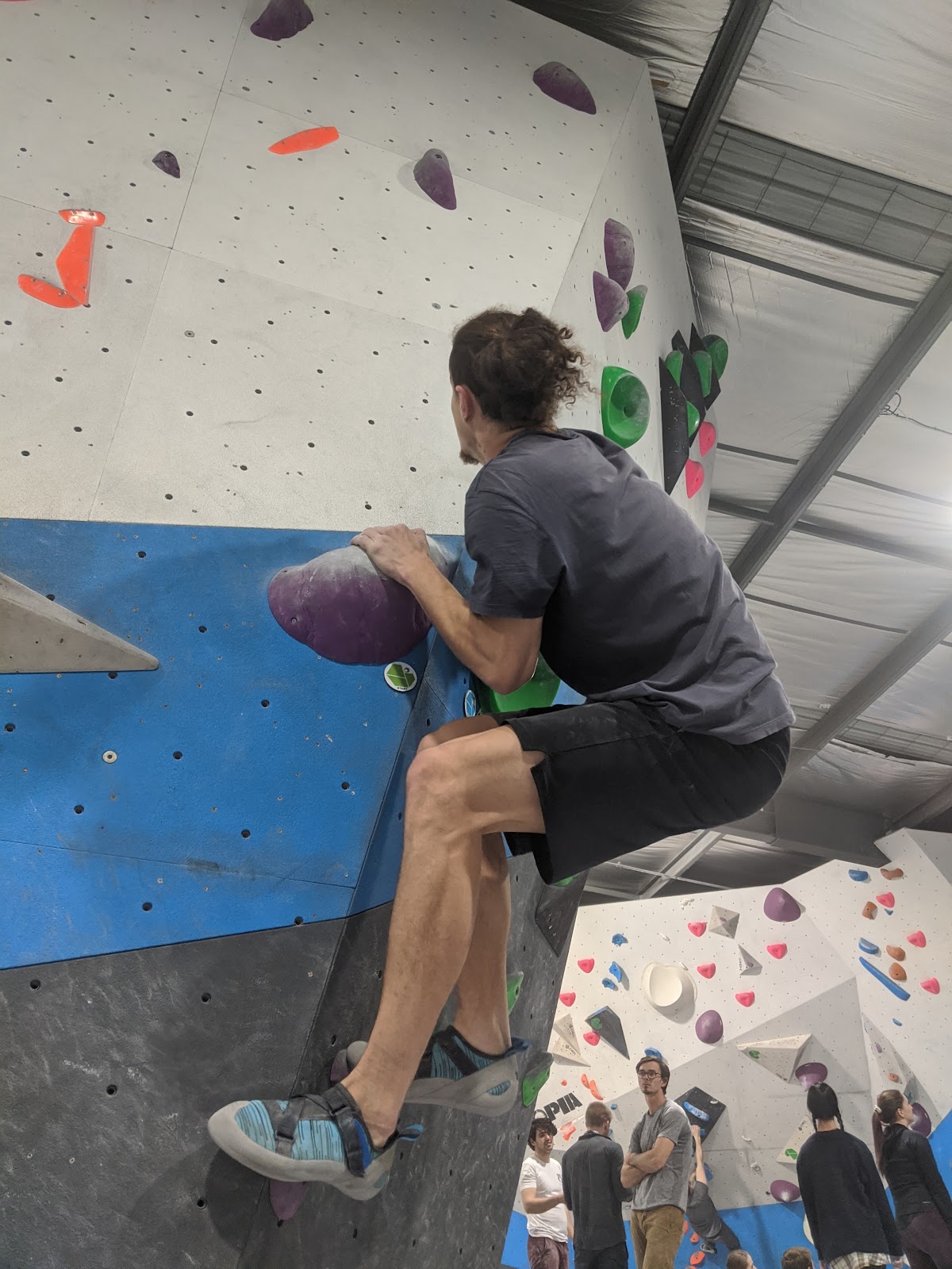 A man is climbing a colorful indoor rock wall in what appears to be a gym setting.