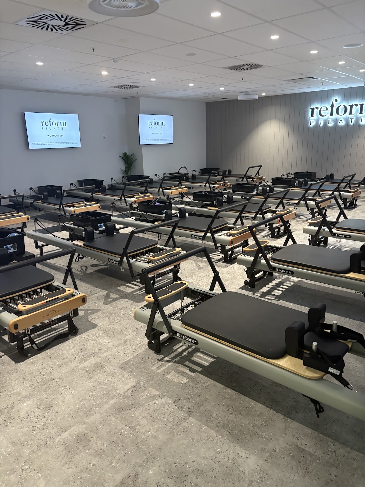 The photo showcases a Pilates studio interior with multiple reformer machines arranged in rows.