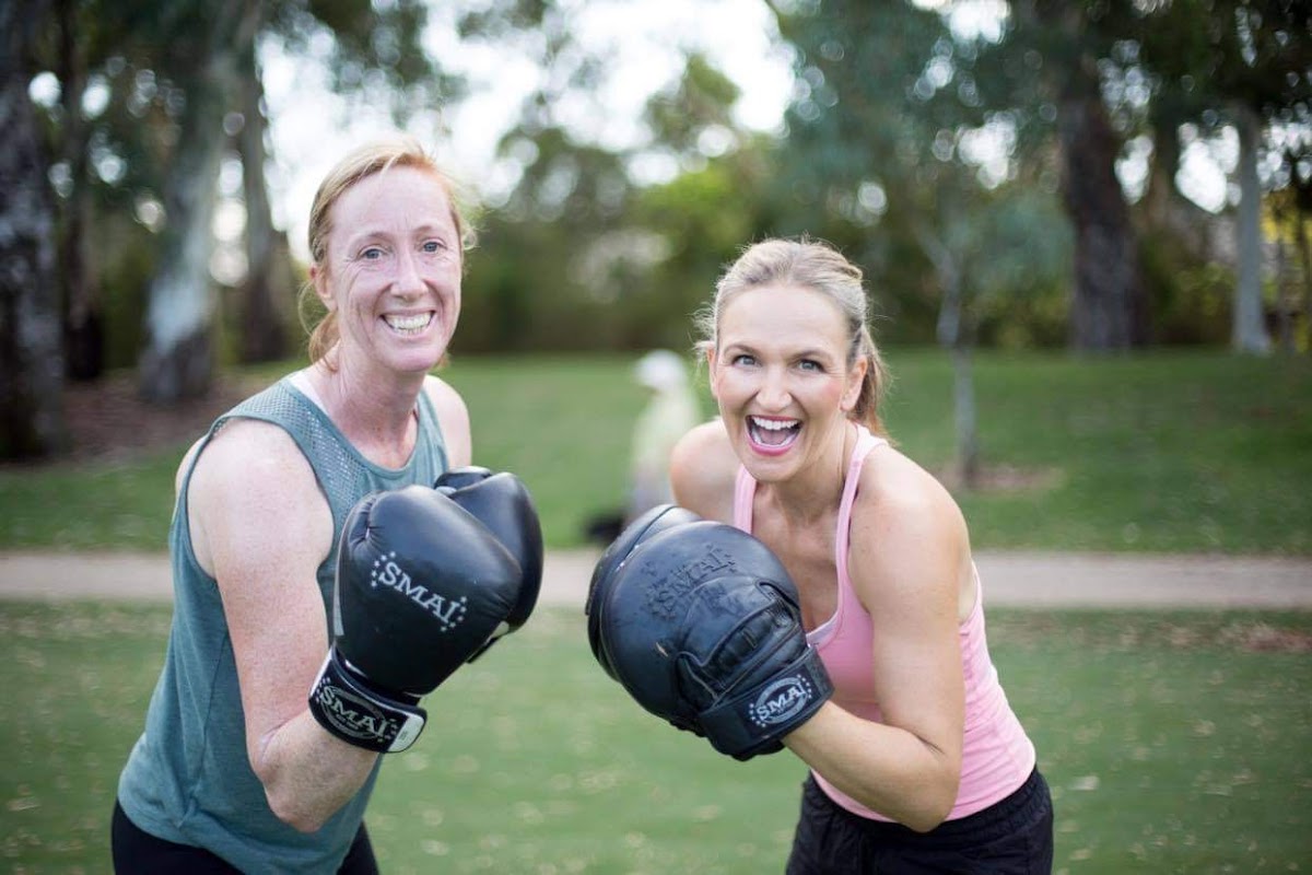 Two smiling women are engaged in an outdoor boxing training session.