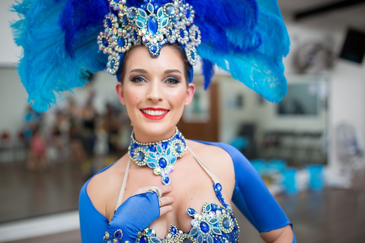 A portrait of a female trainer wearing elaborate blue costume and makeup, likely promoting dance fitness or performance training.
