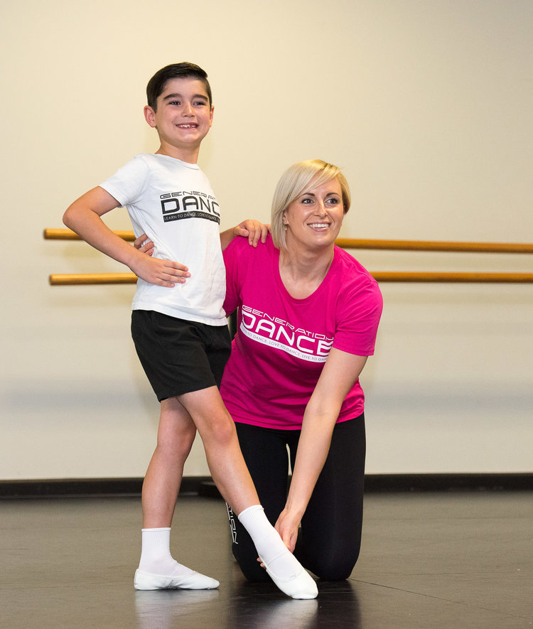 A female trainer is posing with a young boy in a dance studio setting, likely demonstrating or teaching a pose.
