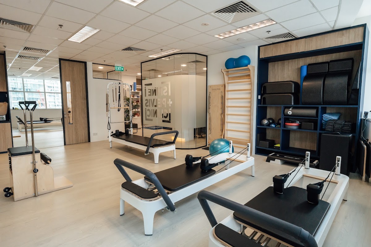 The photo shows a clean and minimalist Pilates studio with several reformer machines and some free weights.