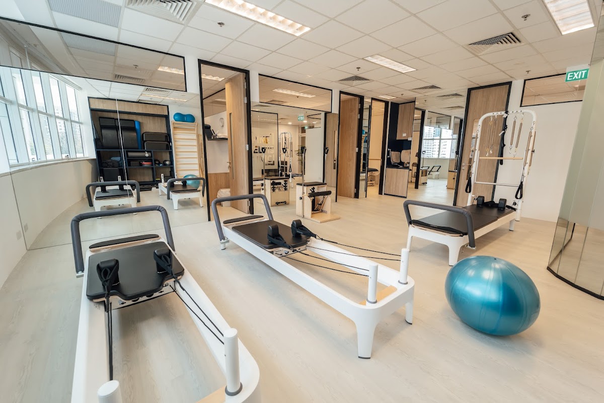 The photo showcases a clean and modern Pilates studio with multiple reformer machines and yoga mats visible.