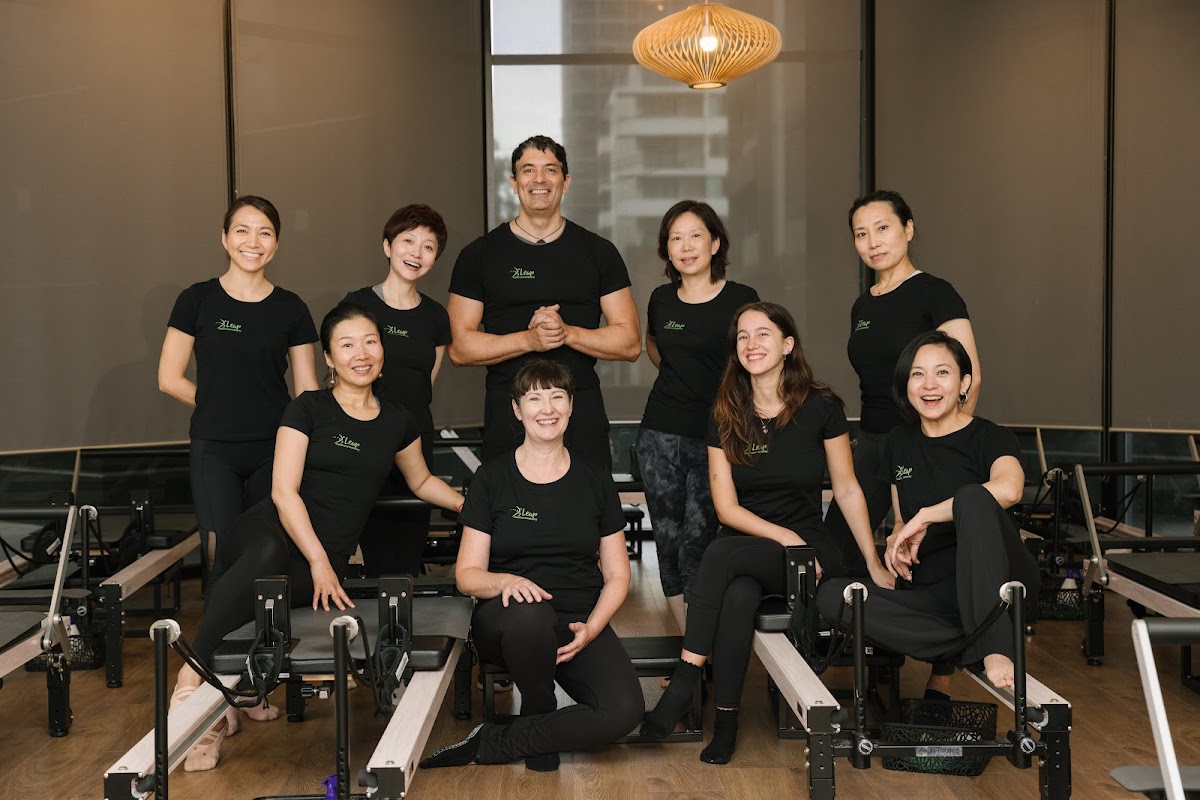 A group of people, including trainers, are posing in a studio setting with reformer pilates machines.