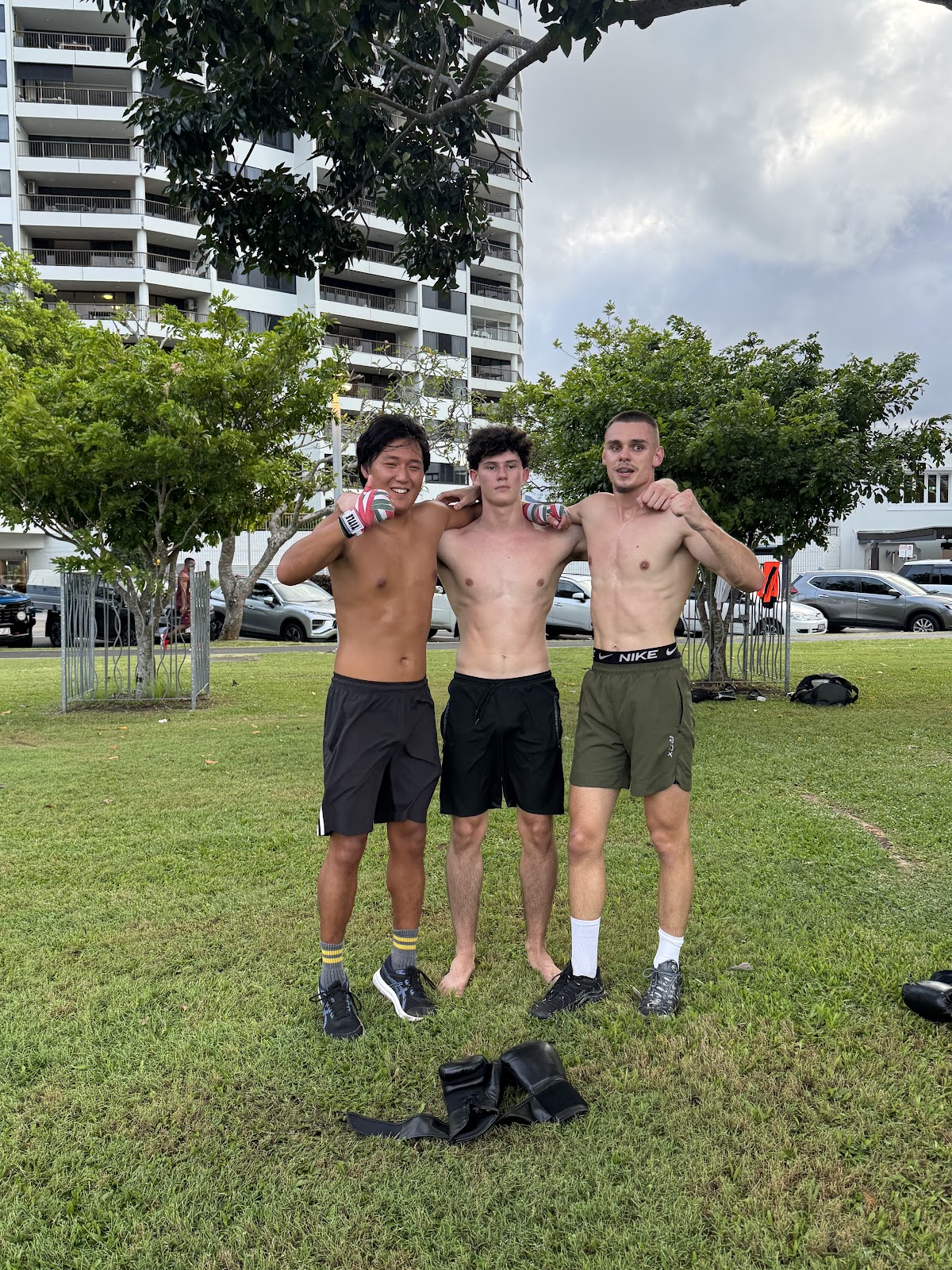 Three men are posing outdoors after a boxing workout with equipment visible on the grass.