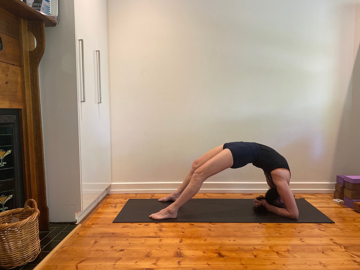A person is performing a yoga pose on a mat in a room with a fireplace and wooden floors.