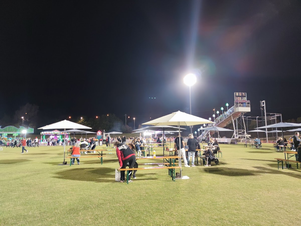 A large group of people are participating in an outdoor bootcamp-style workout on a grassy field at night, illuminated by bright lights and umbrellas.